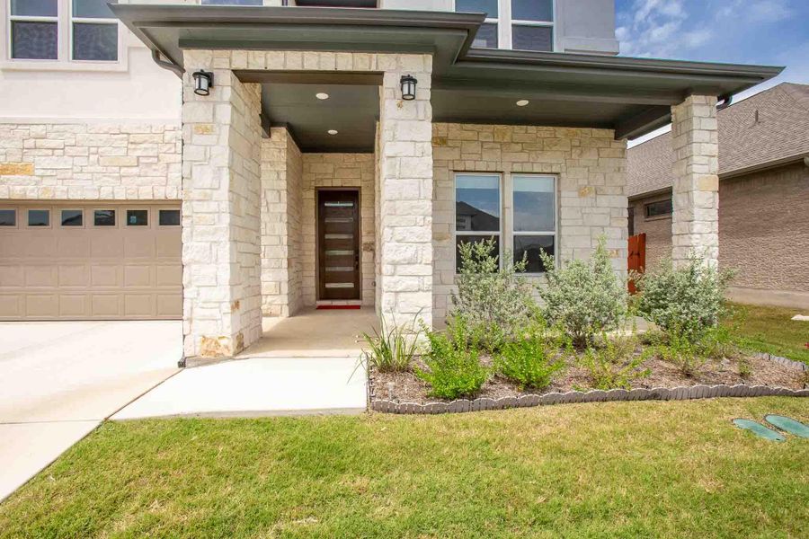 Stone facade with a covered entry, featuring a modern dark wood-finish front door