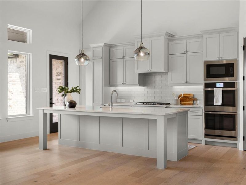 Kitchen with tasteful backsplash, light wood finished floors, stainless steel appliances, a kitchen island with sink, and decorative light fixtures Kitchen with tasteful backsplash, light wood finished floors, stainless steel appliances, a kitchen island with sink, and decorative light fixtures