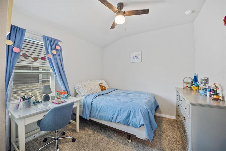 Carpeted bedroom with vaulted ceiling, ceiling fan, and a desk