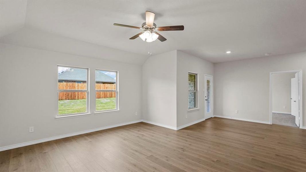 Spacious interior room featuring wood-finish flooring, vaulted ceiling, and a ceiling fan with light fixture