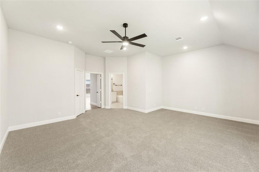 Spacious empty bedroom with gray carpet, ceiling fan, and ensuite bathroom doorway visible