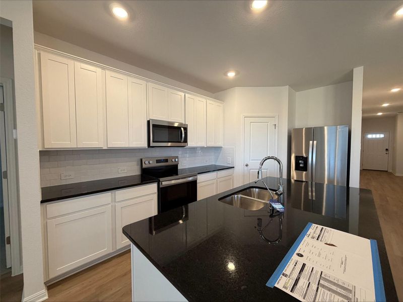 Kitchen featuring appliances with stainless steel finishes, light wood finished floors, dark stone countertops, and recessed lighting