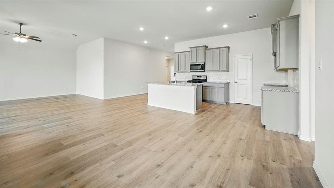 Kitchen with gray cabinetry, open floor plan, a kitchen island with sink, backsplash, and recessed lighting