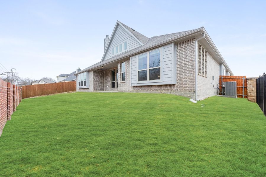 Rear exterior of two-story brick home with large windows, green lawn, and wood privacy fence Rear exterior of two-story brick home with large windows, green lawn, and wood privacy fence