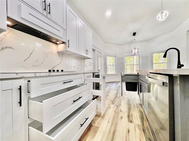 White Shaker Drawers in Several Sizes tucked under the Ge Electric Cook-Top to Maximize Storage Space including a Hidden Spice Rack for Fast and Easy Access when prepping those delicious home cooked meals plus a Hidden Shaker Drawer for the Trash Can no one wants lingering around.