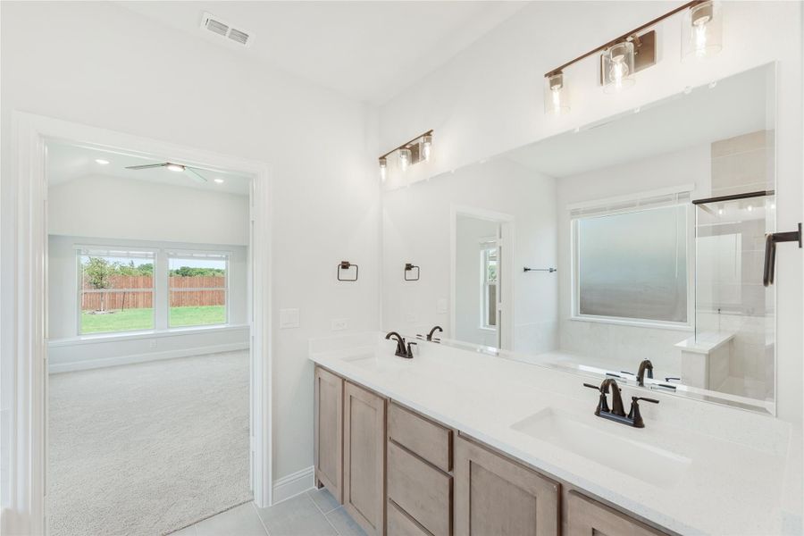 Ensuite bathroom with double vanity, white countertops, large mirror, and glass shower, open to carpeted bedroom.