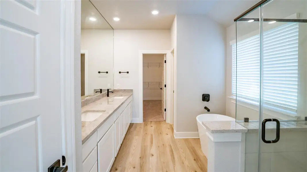 Full bath featuring double vanity, light wood-style floors, a stall shower, a freestanding tub, and a spacious closet Full bath featuring double vanity, light wood-style floors, a stall shower, a freestanding tub, and a spacious closet