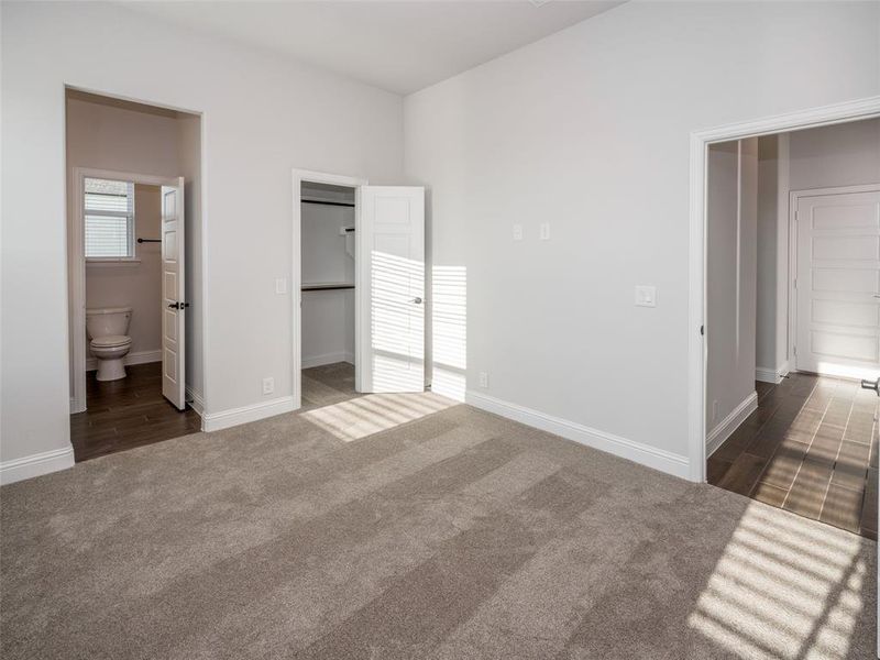 Unfurnished bedroom featuring a spacious closet, dark carpet, and ensuite bathroom