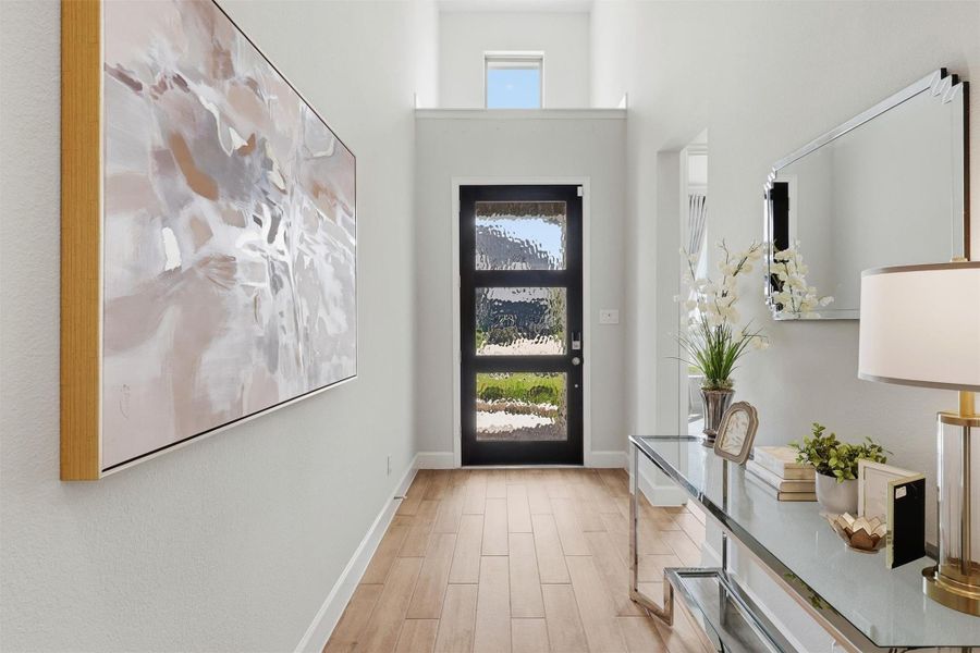 An impressive two-story foyer creates a memorable first impression with soaring ceilings, abundant natural light, designer wood-look tile flooring, and a striking modern front door featuring textured glass for both style and privacy.