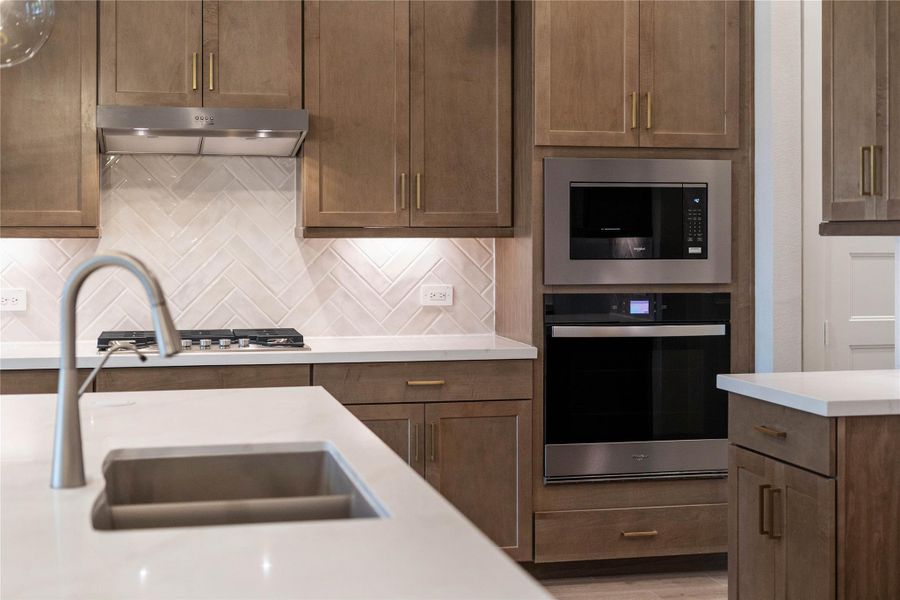 Whirlpool stainless steel appliances including 30-inch gas cooktop, vent hood, sensor cooking microwave, single wall oven with air fry capability and large capacity dishwasher. The stylish white backsplash tile extends from the countertop to the upper cabinets, adding texture and visual interest.