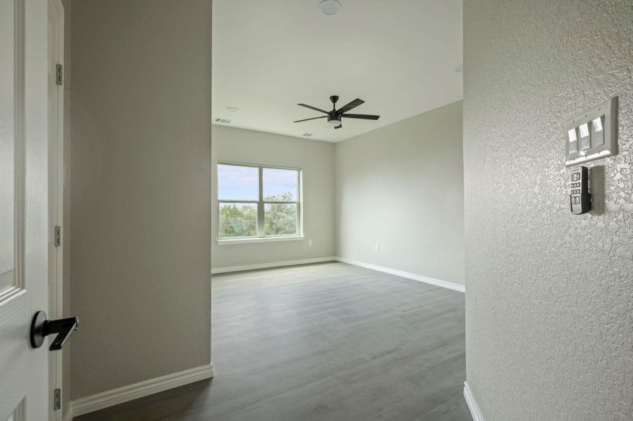 Empty room with a textured wall, wood finished floors, and a ceiling fan