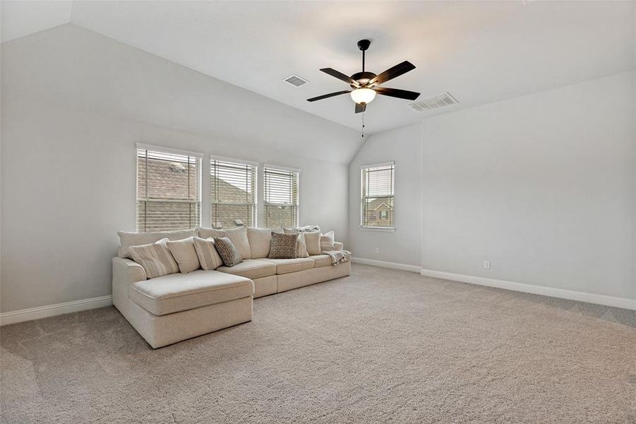 Spacious room featuring vaulted ceilings, neutral-toned carpeting, multiple windows with blinds, and a ceiling fan with integrated lighting