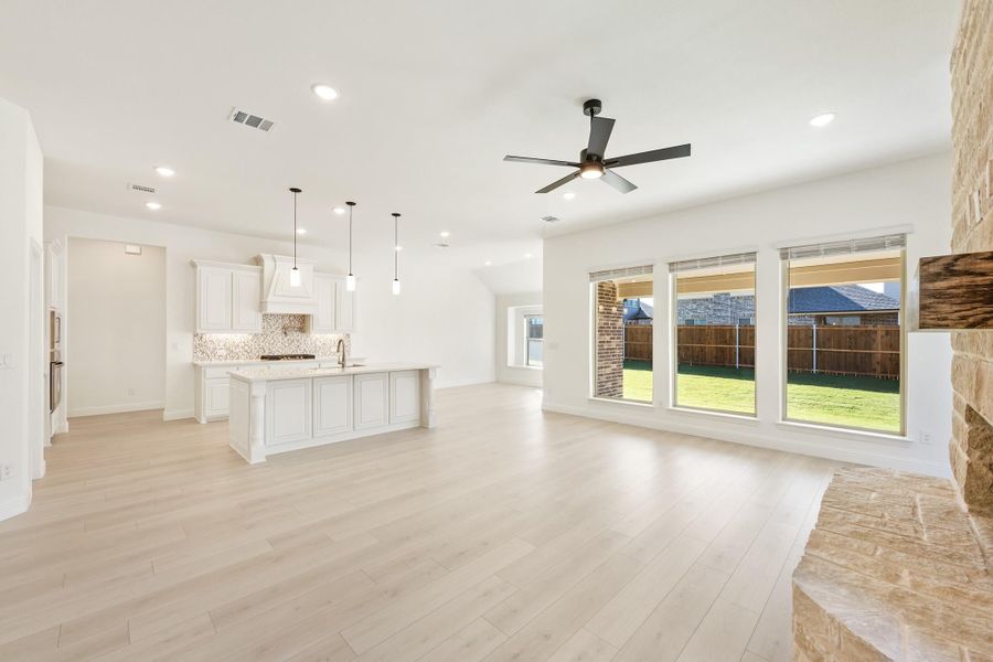 Open-concept living area with light wood floors, ceiling fan, and white kitchen with island and pendant lights Open-concept living area with light wood floors, ceiling fan, and white kitchen with island and pendant lights