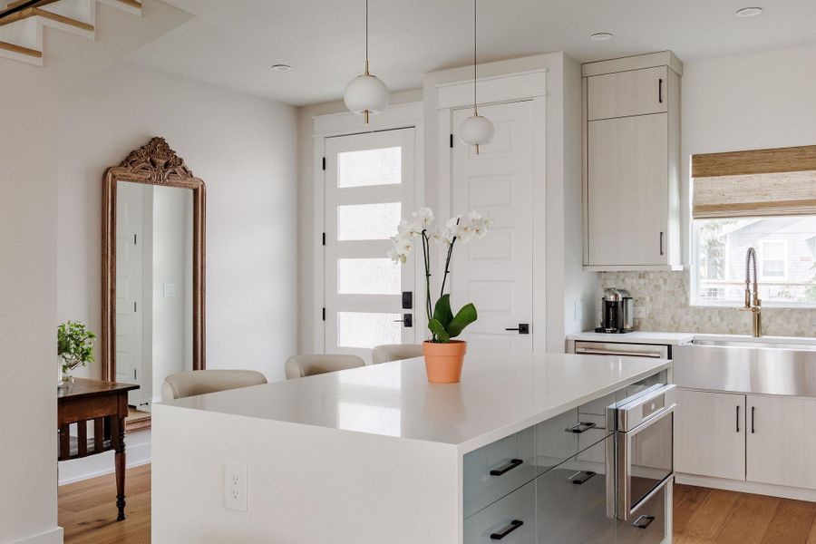 Two tone kitchen with light wood-style flooring, a kitchen island, two tone color scheme, hanging light fixtures, and light stone countertops