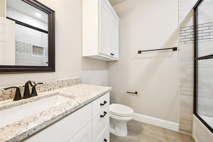 Full bathroom featuring vanity, a shower with shower door, and wood finished floors Full bathroom featuring vanity, a shower with shower door, and wood finished floors
