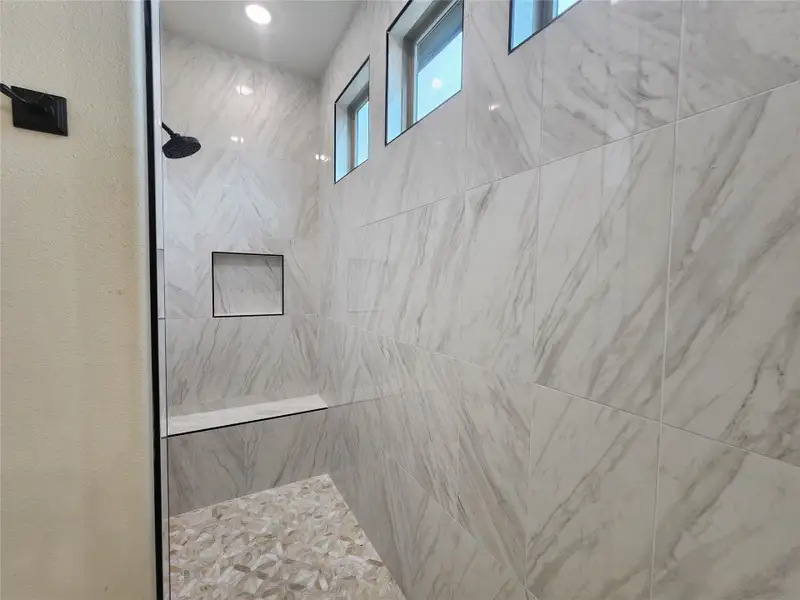 Walk-in shower featuring large format tile walls, recessed niche, integrated bench, and mosaic tile flooring