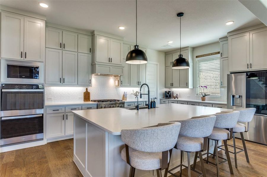 Kitchen with dark wood finished floors, tasteful backsplash, appliances with stainless steel finishes, decorative light fixtures, and an island with sink Kitchen with dark wood finished floors, tasteful backsplash, appliances with stainless steel finishes, decorative light fixtures, and an island with sink