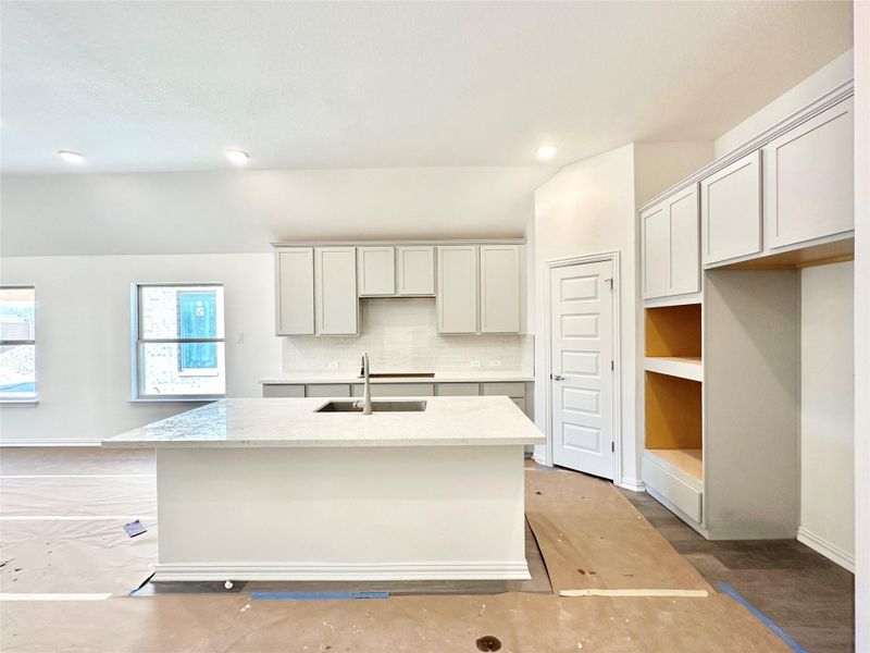 Kitchen featuring decorative backsplash, a kitchen island with sink, light stone countertops, and recessed lighting