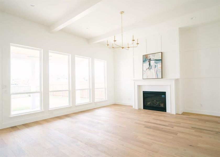 Unfurnished living room with a notable chandelier, light hardwood / wood-style flooring, and vaulted ceiling with beams