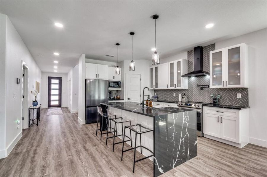 Kitchen featuring wall chimney range hood, stainless steel appliances, a kitchen breakfast bar, light wood-style flooring, and recessed lighting