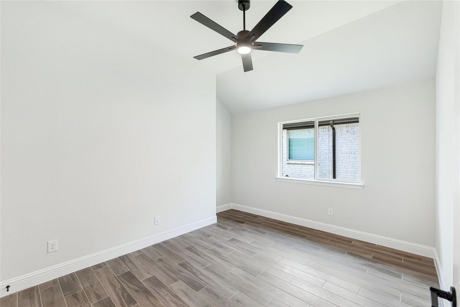 Empty bedroom with vaulted ceiling, black ceiling fan, wood-look tile floors, and a single window Empty bedroom with vaulted ceiling, black ceiling fan, wood-look tile floors, and a single window