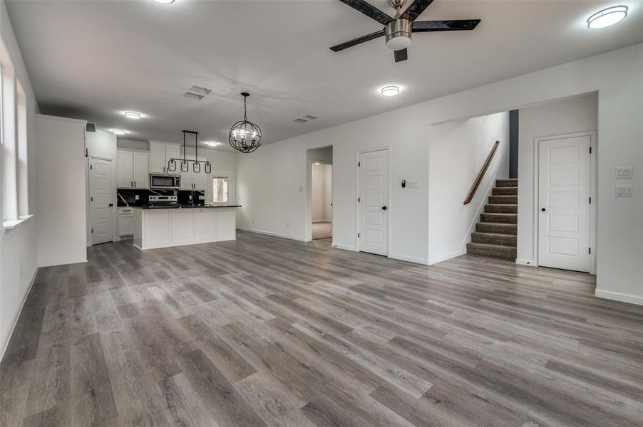 Unfurnished living room with ceiling fan with notable chandelier and light wood-type flooring