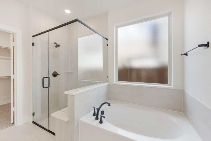 Bathroom with soaking tub, glass-enclosed walk-in shower, tile walls, and frosted window next to walk-in closet