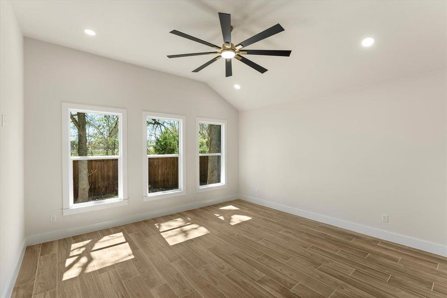 Primary bedroom with wood look tile floors, lofted ceiling, recessed lighting, and a ceiling fan
