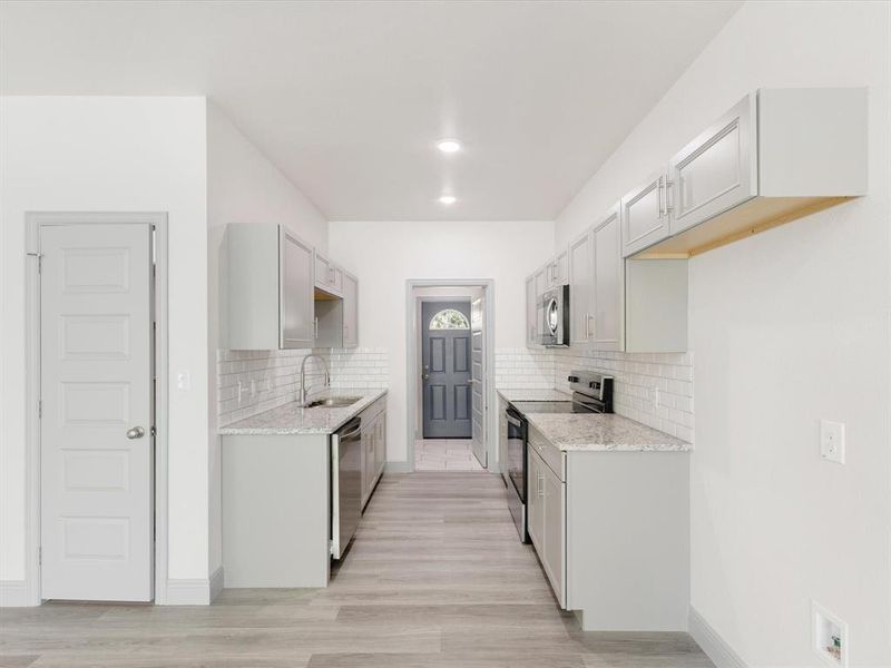 Kitchen featuring stainless steel appliances, light stone counters, decorative backsplash, and light wood-style flooring
