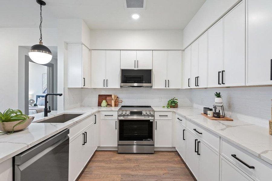Kitchen featuring stainless steel appliances, light stone countertops, light wood-style flooring, tasteful backsplash, and decorative light fixtures