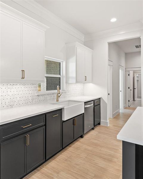 Kitchen featuring two tone cabinetry, light wood-style flooring, ornamental molding, light stone counters, and backsplash