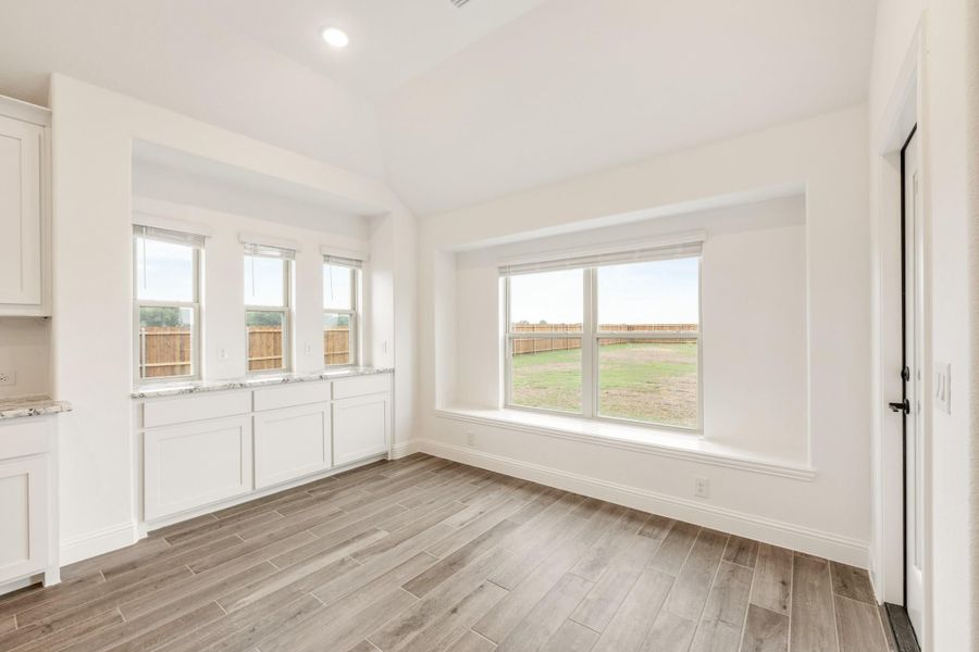 Empty dining area with wood-look tile floors, white walls, and large windows overlooking a fenced backyard