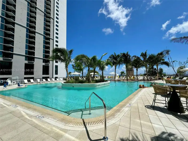 Outdoor swimming pool featuring a central island with palm trees, stone-tile decking, and metal handrails