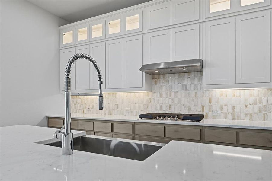 Kitchen with glass insert cabinets, light stone counters, backsplash, and white cabinetry