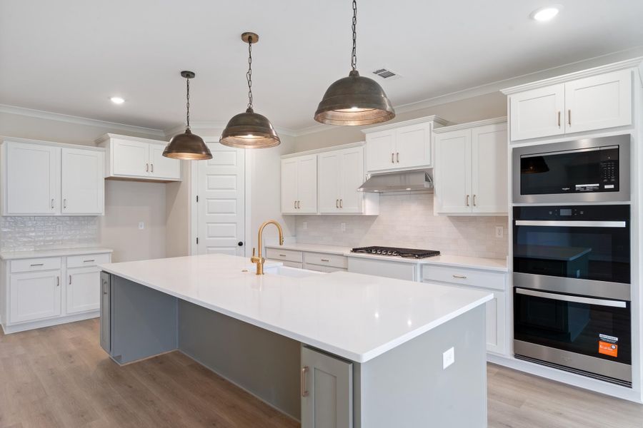 Kitchen featuring a large island with white countertop, brass-finish faucet, and three pendant lights Kitchen featuring a large island with white countertop, brass-finish faucet, and three pendant lights