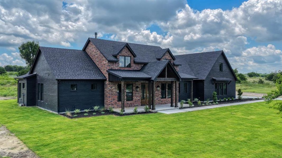 Modern farmhouse exterior featuring dark brick and horizontal siding, a covered entry with timber posts, dark-shingle roofing, and manicured landscaping beds