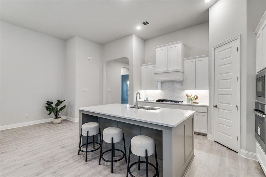 Kitchen featuring backsplash, a center island with sink, white cabinetry, and sink