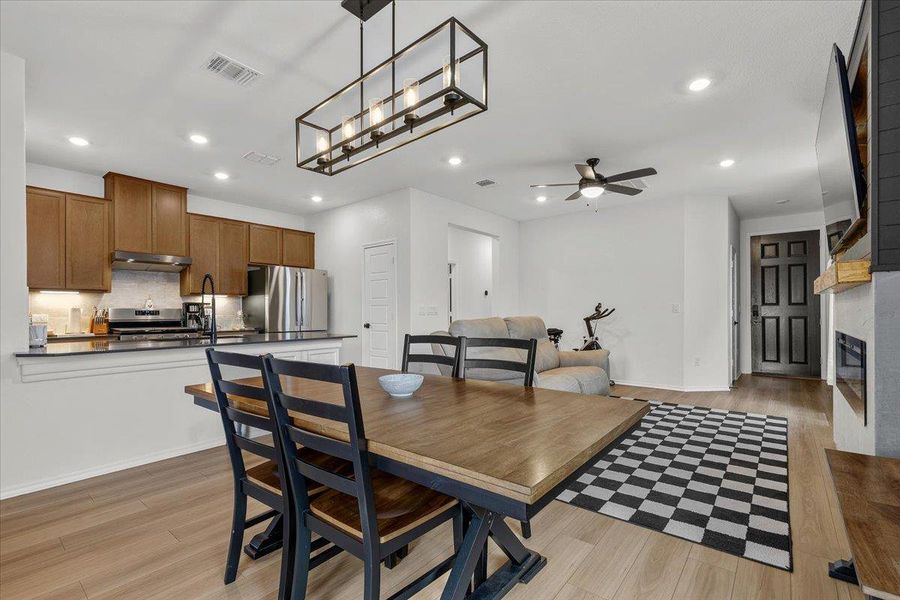 An open-concept living space presents a seamless flow between the kitchen and dining area, accented by a contemporary rectangular chandelier.