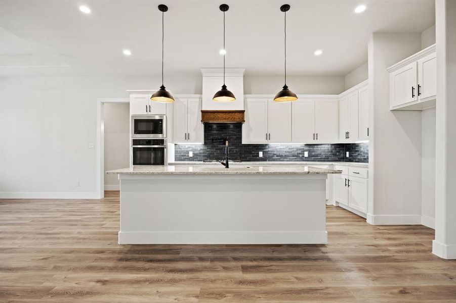 Kitchen featuring a center island with sink, white cabinets, and oven