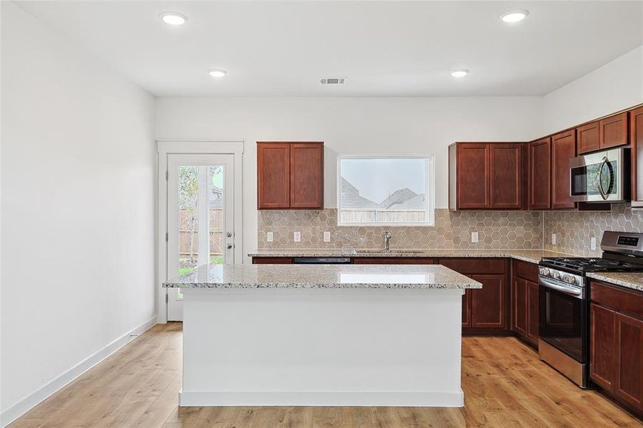 Kitchen with light hardwood / wood-style floors, a center island, and stainless steel appliances