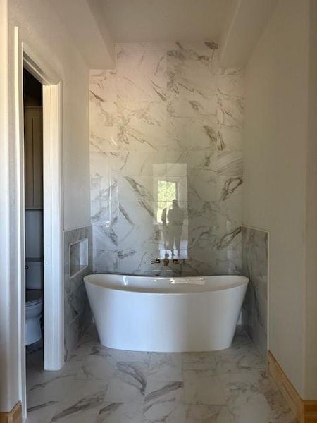 Bathroom with tile walls, a freestanding tub, light marble finish flooring, and stone wall