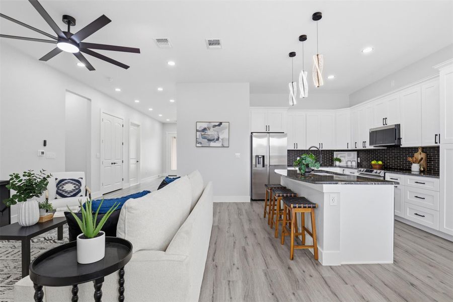Open-concept kitchen featuring white shaker cabinetry, dark granite countertops, stainless steel appliances, and a black mosaic tile backsplash
