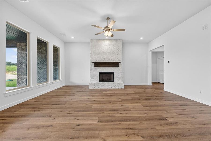 Spacious living area featuring wood-finish flooring, a white brick fireplace with a dark wood mantel, and a ceiling fan