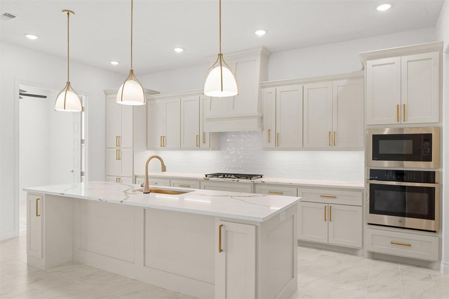 Kitchen with stainless steel appliances, light stone counters, hanging light fixtures, a center island with sink, and light marble finish flooring