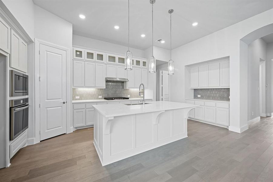 Kitchen featuring backsplash, white cabinetry, a breakfast bar area, an island with sink, and arched walkways Kitchen featuring backsplash, white cabinetry, a breakfast bar area, an island with sink, and arched walkways