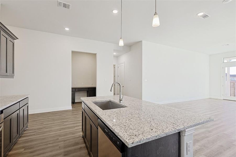 Kitchen with light stone countertops, sink, stainless steel dishwasher, pendant lighting, and a center island with sink