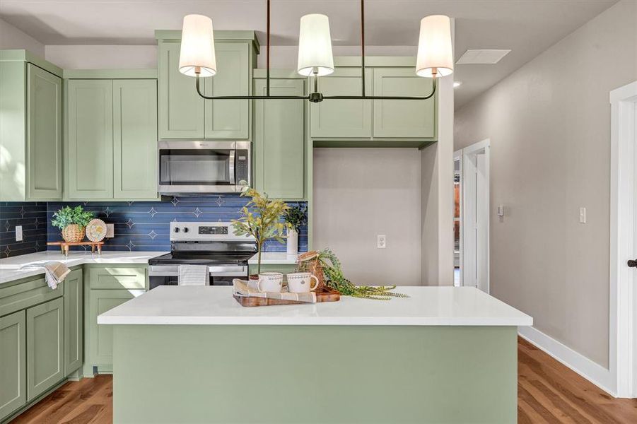 Kitchen with green cabinets, decorative backsplash, stainless steel appliances, a kitchen island, and light wood finished floors Kitchen with green cabinets, decorative backsplash, stainless steel appliances, a kitchen island, and light wood finished floors