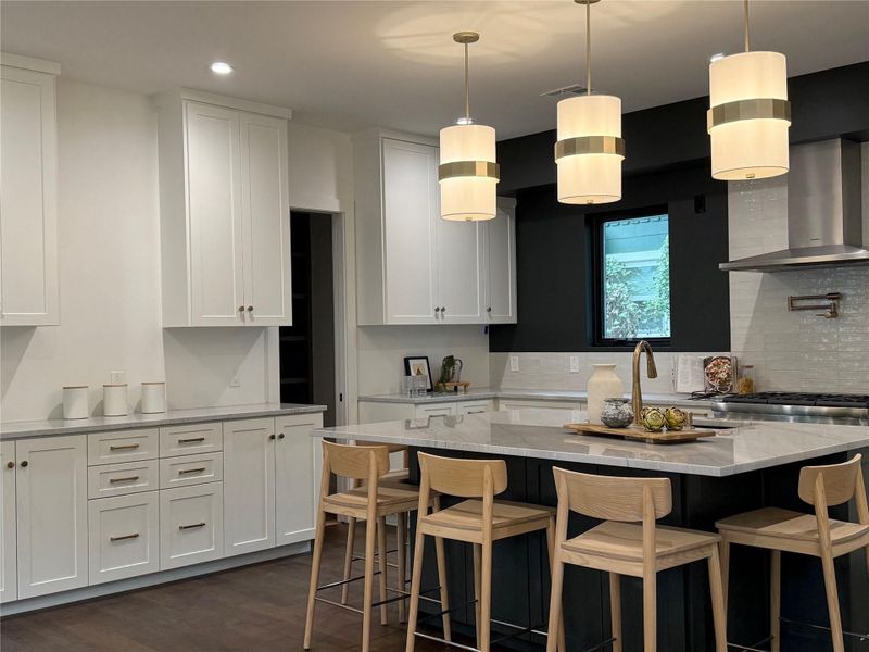 Kitchen with wall chimney exhaust hood, hanging light fixtures, light stone countertops, a kitchen breakfast bar, and recessed lighting Kitchen with wall chimney exhaust hood, hanging light fixtures, light stone countertops, a kitchen breakfast bar, and recessed lighting