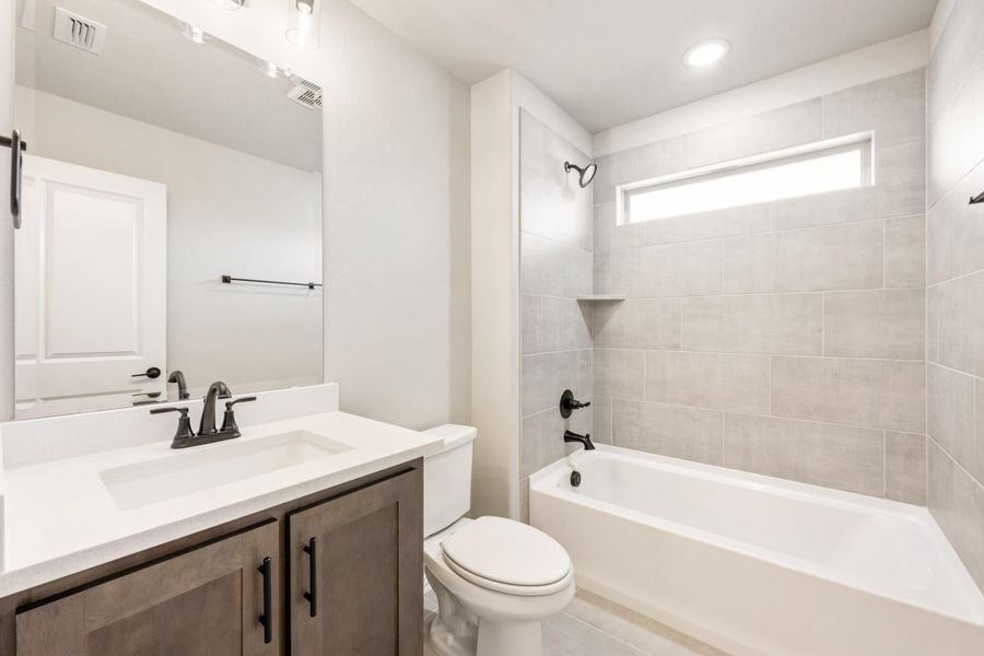 Full bathroom with dark wood vanity, white countertop, soaking tub, and tiled shower surround with small window