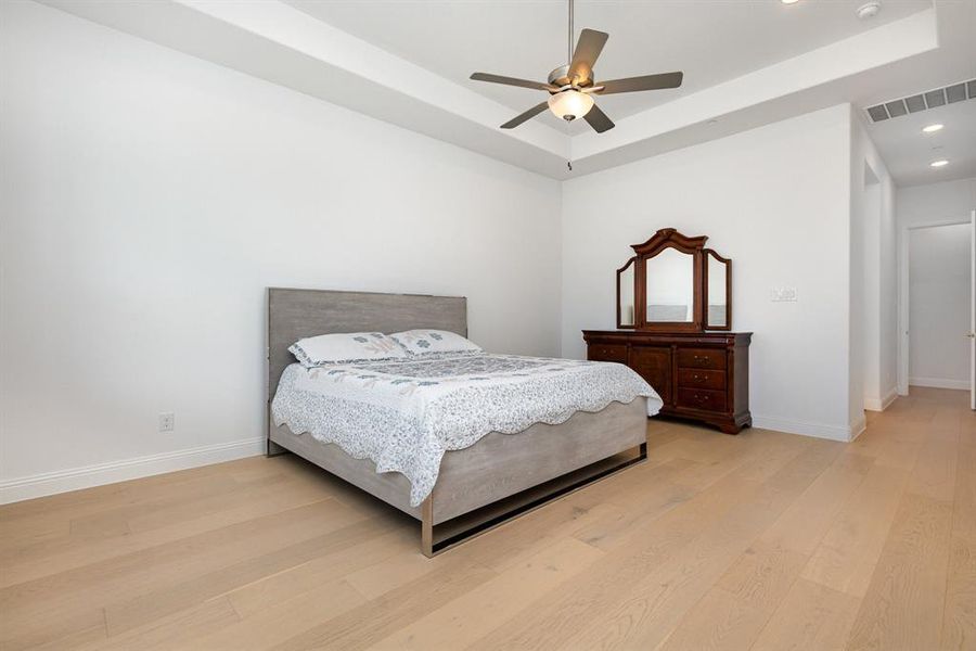Bedroom with a raised ceiling, light wood finished floors, ceiling fan, and recessed lighting